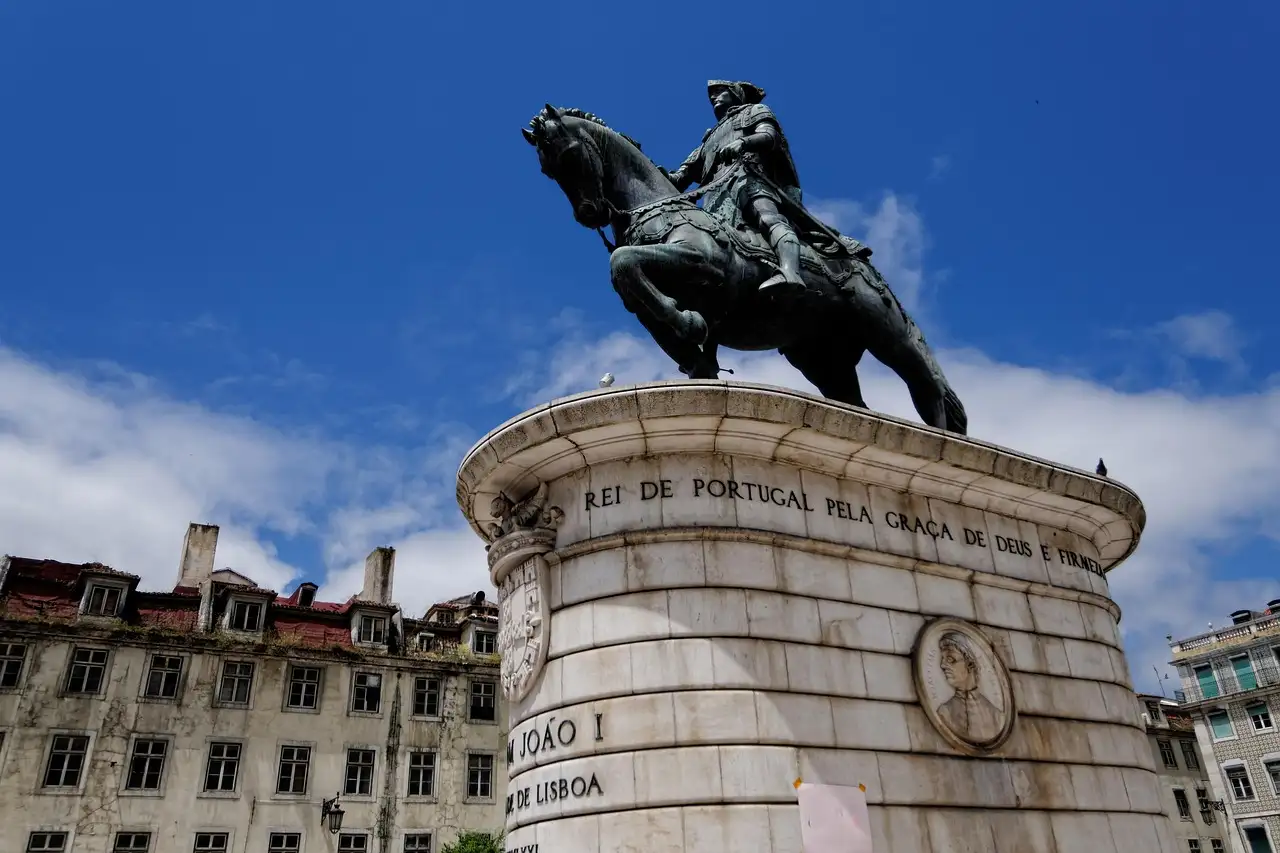 The bronze equestrian statue of King João I on its stone base in Praça da Figueira, Lisbon, against a blue sky