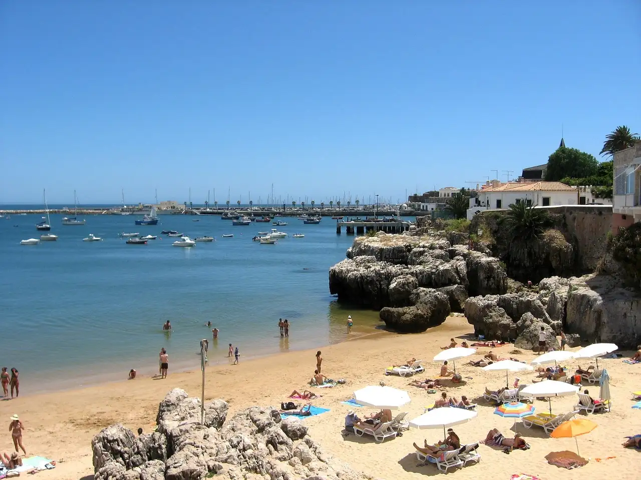Cascais bay with a small sandy beach, rocks and boats moored on the blue water
