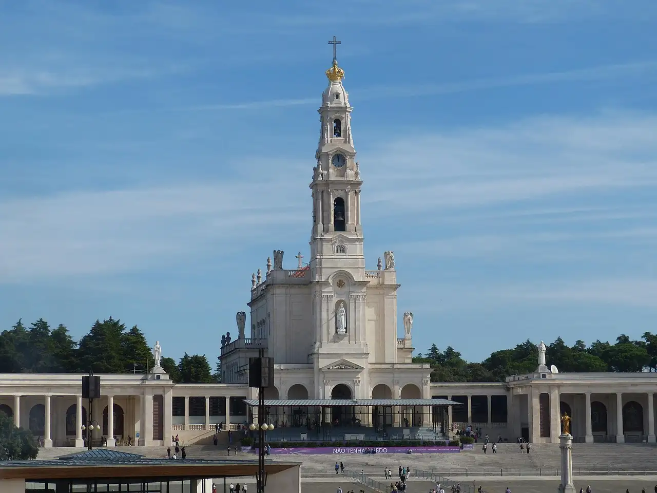 The tall white basilica tower of the Sanctuary of Fátima framed by curved colonnades
