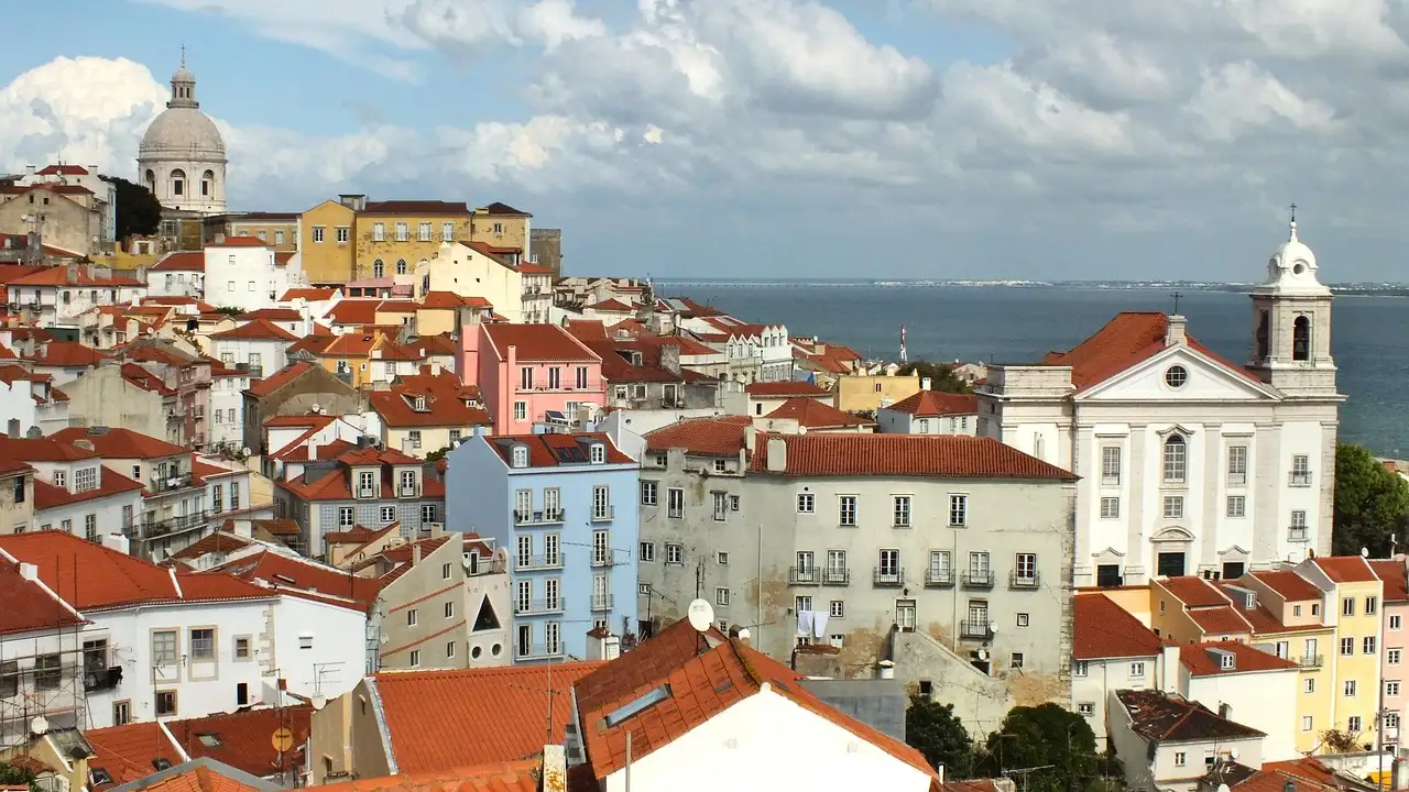 Alfama's terracotta rooftops and church domes with the Tagus river beyond, seen from a Lisbon miradouro