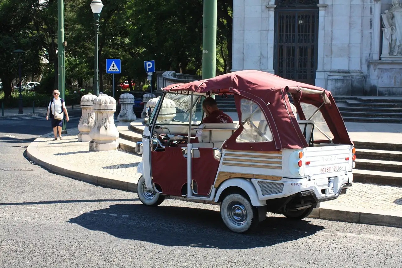 A white and maroon tuk-tuk parked on a Lisbon street beside a historic stone building