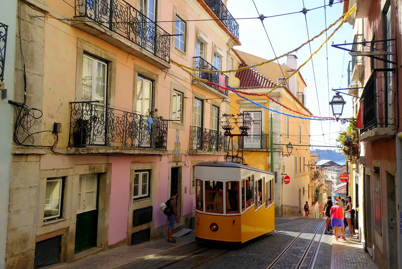 Pastel Lisbon facades with iron balconies on a narrow street, a yellow tram in the distance