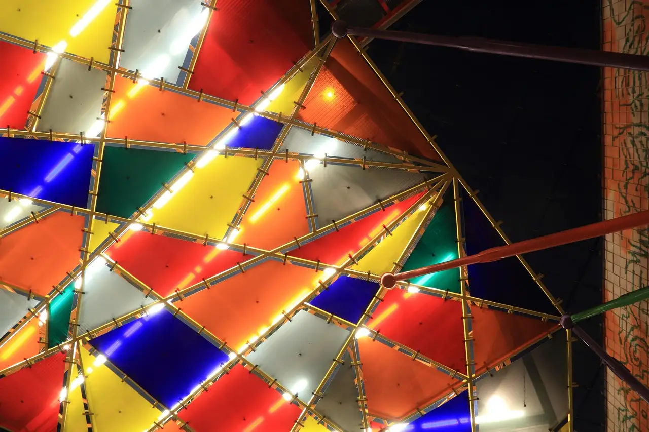 Red, yellow, blue, green and white glass panels lit from behind in a steel-framed canopy above a Lisbon metro station at night
