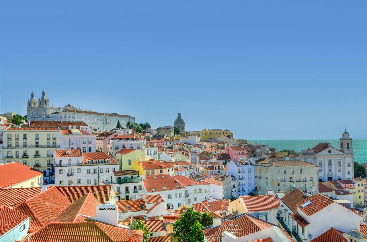 Terracotta roofs and pastel houses of Alfama in Lisbon stepping down towards the Tagus under a clear blue sky