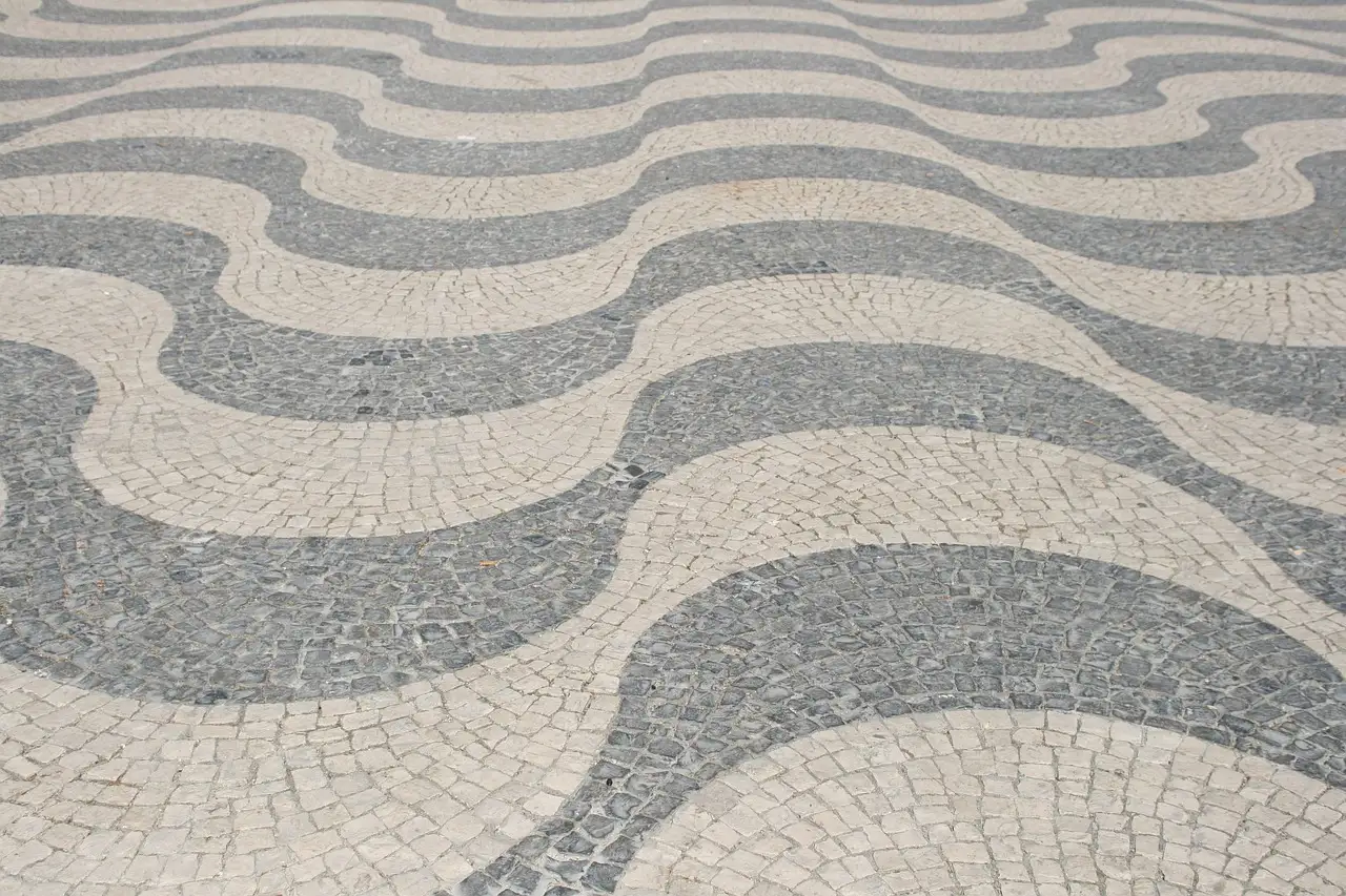 A wave pattern of pale limestone and grey basalt cobbles in a Lisbon pavement, filling the whole frame