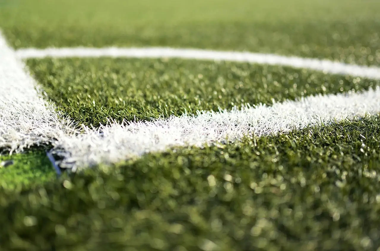 The white painted corner lines of a football pitch on short green grass, photographed close to the ground with a soft blurred background