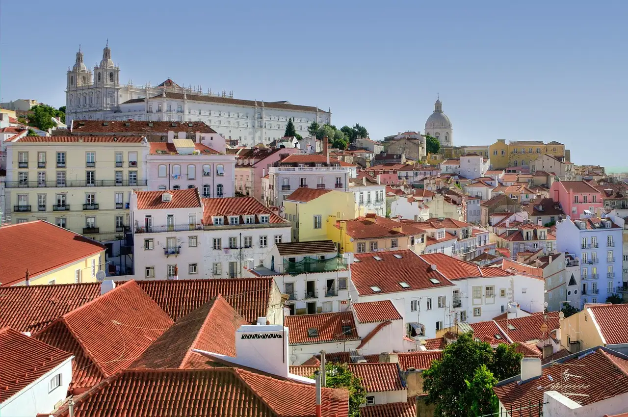 Orange-tiled Alfama rooftops with the white domes of São Vicente and Santa Engrácia under a blue sky