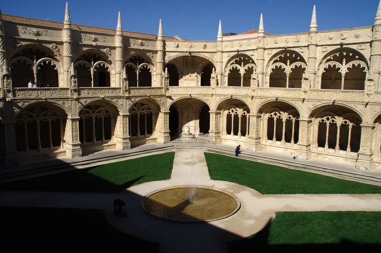 Sunlit arched cloister of Jerónimos Monastery around its green courtyard in Belém