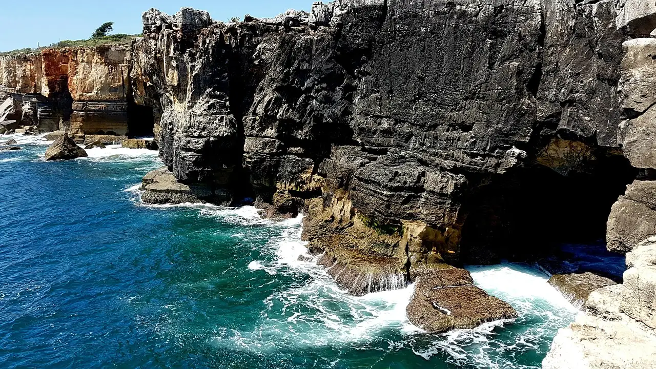Rugged cliffs and cave openings above turquoise Atlantic surf on the Cascais coast