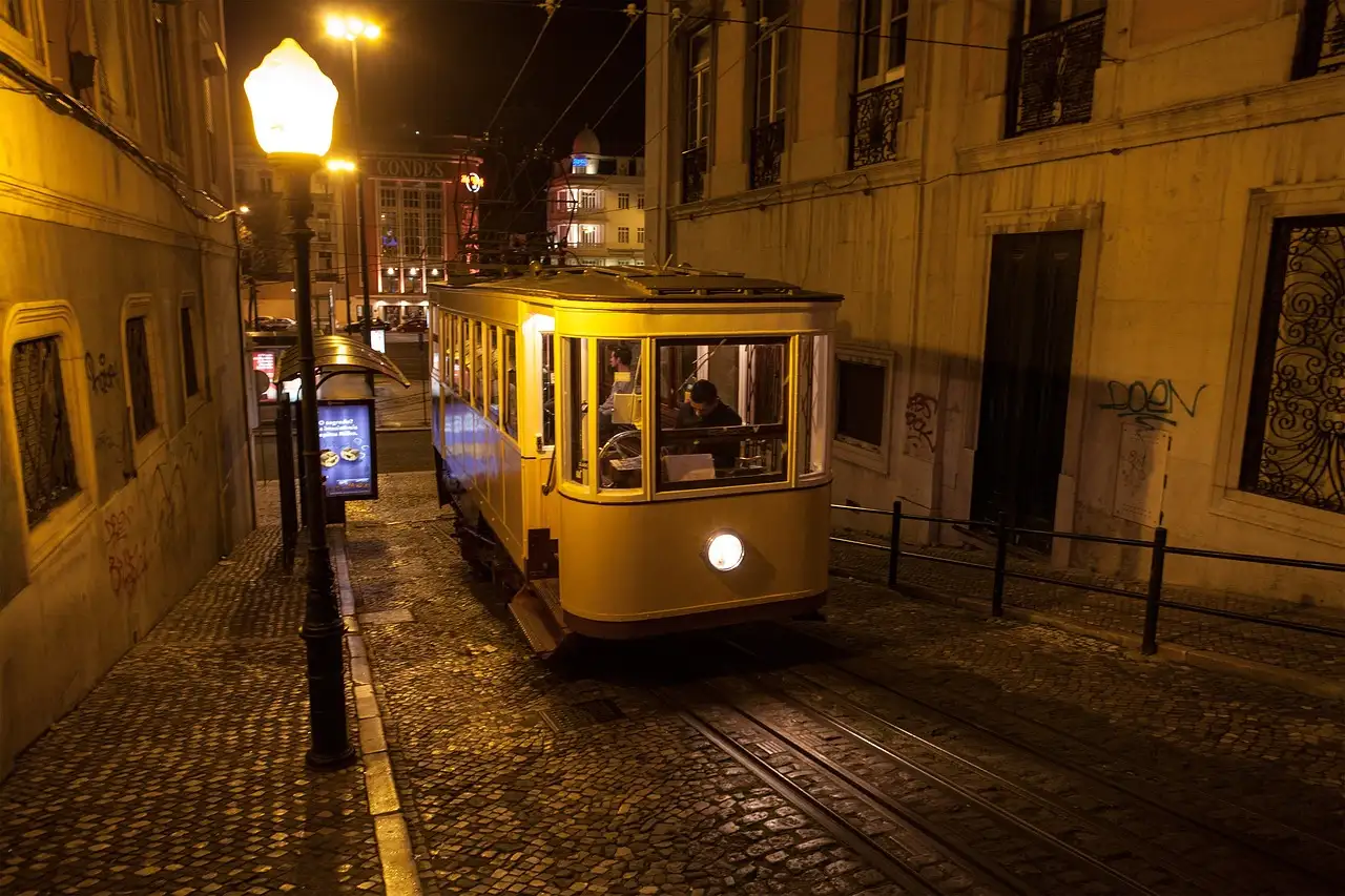 Yellow tram on a narrow cobbled Lisbon street at night under a lamp