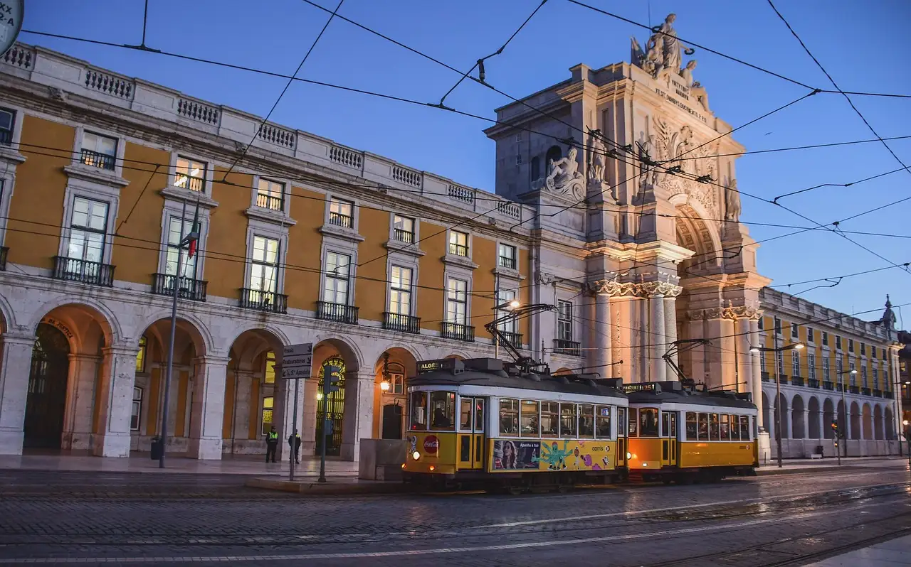 Yellow Lisbon tram in front of the arcaded facade of Praça do Comércio at dusk
