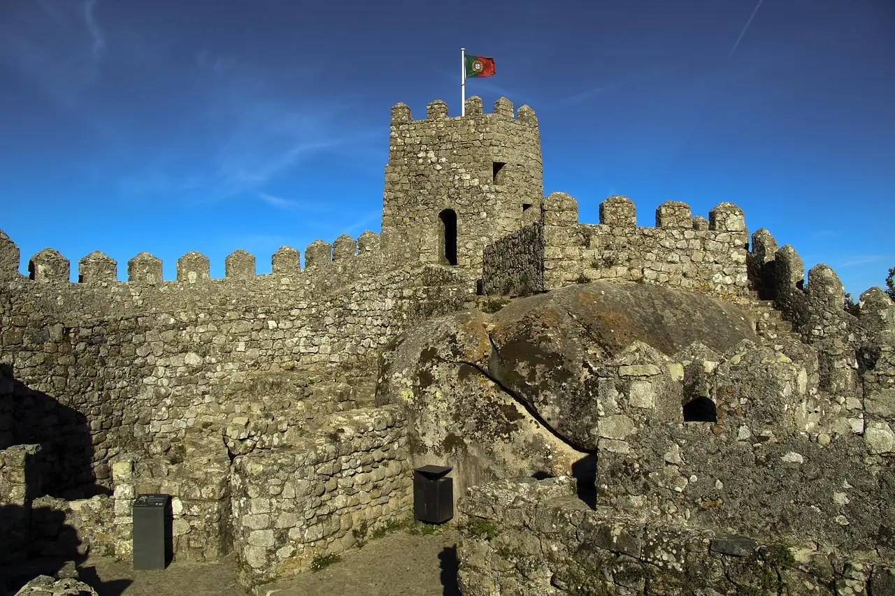 Stone tower and battlements of the Castle of the Moors in Sintra, with a flag against a blue sky