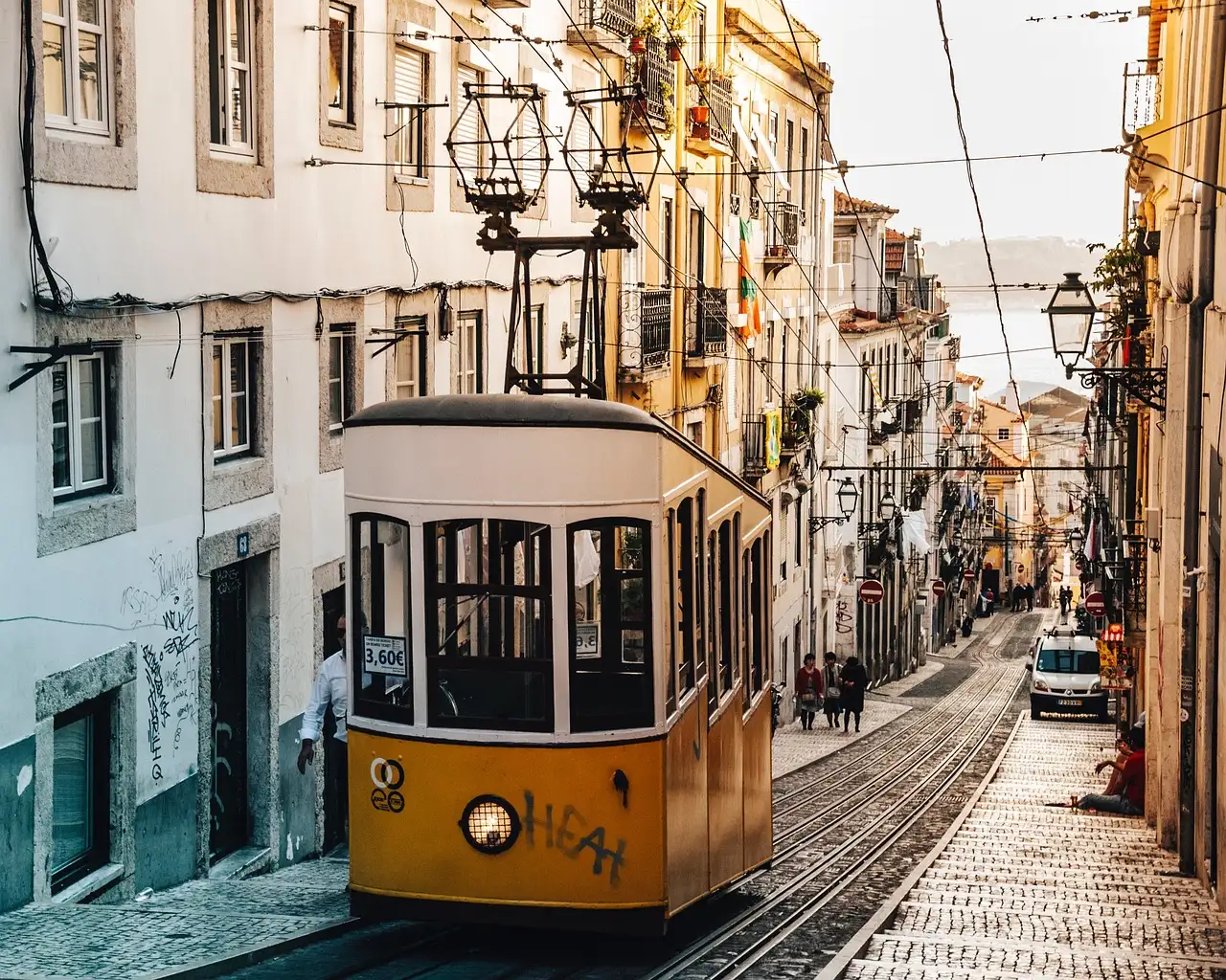 Yellow tram climbing a steep cobbled street between tall old houses in Lisbon