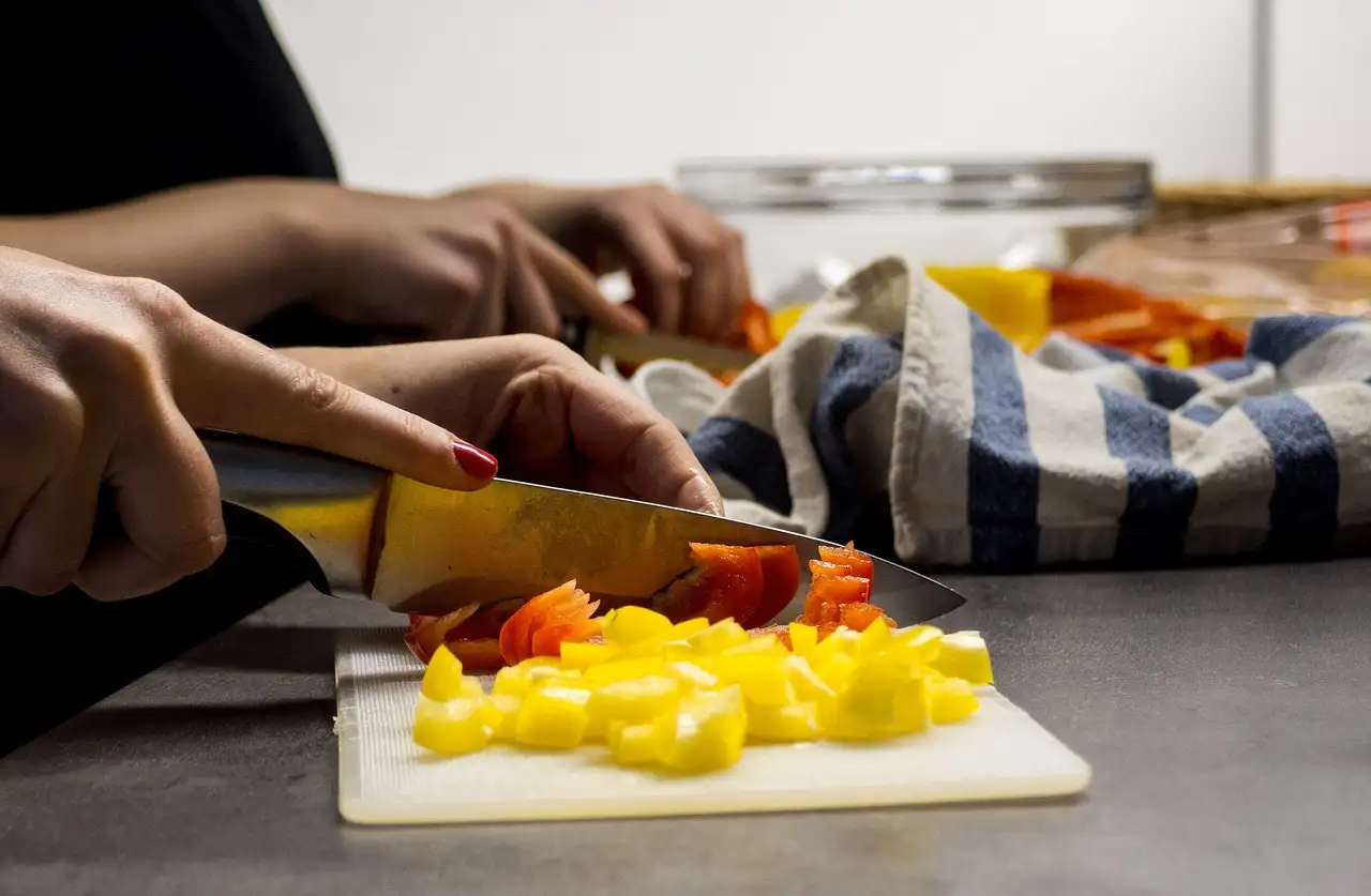 Hands chopping yellow peppers with a knife on a kitchen board