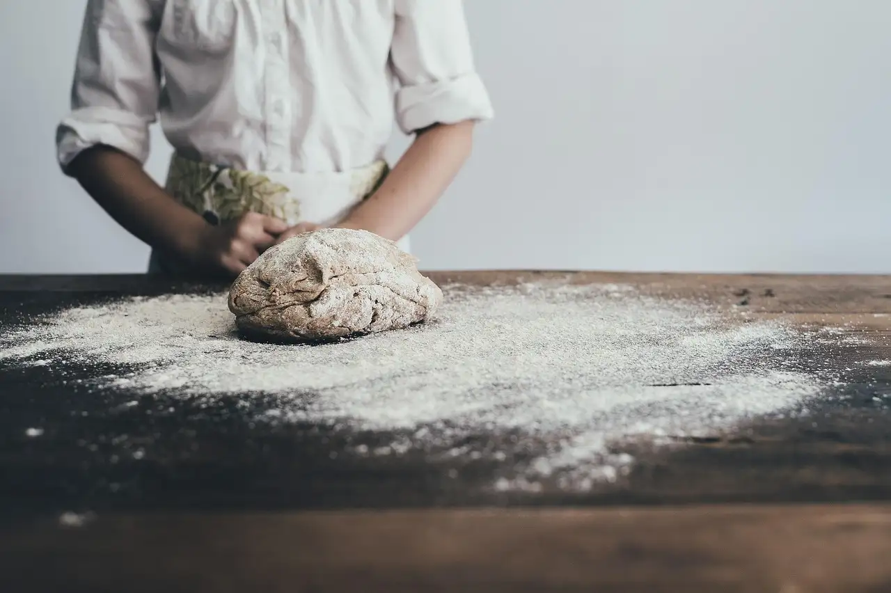 A baker's hands working dough on a floured wooden surface