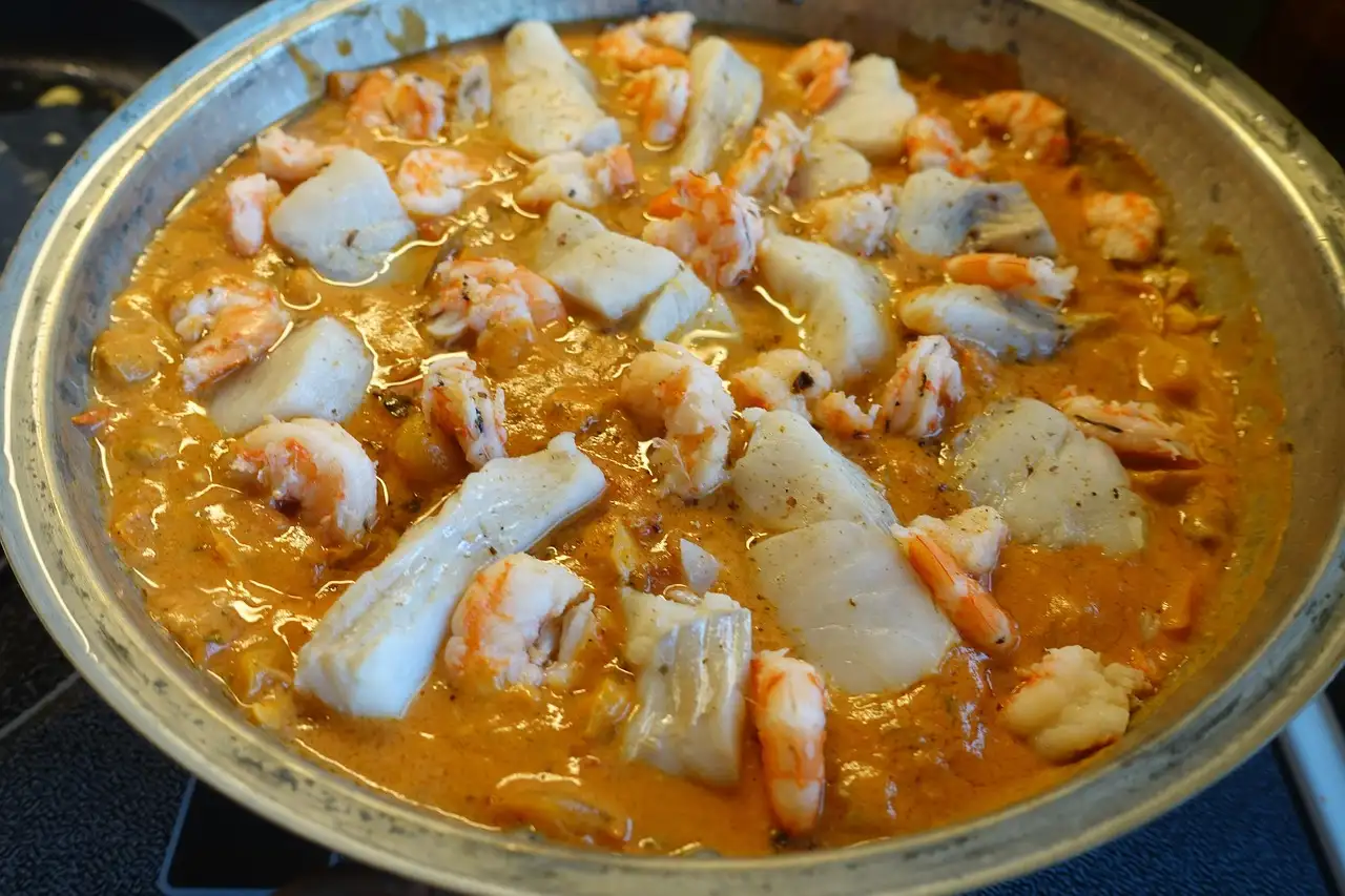 Portuguese cataplana of fish and prawns in a rich orange sauce in a copper-rimmed pan