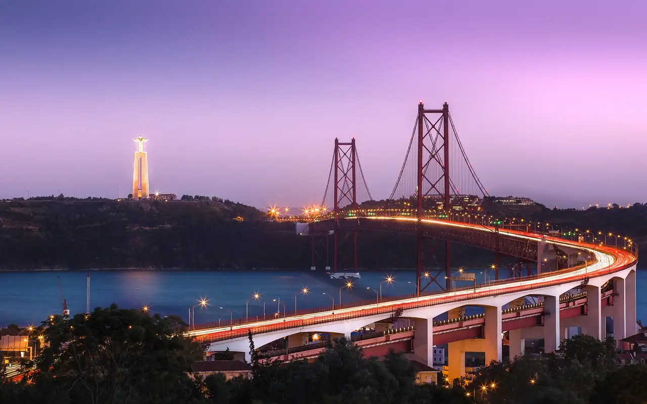 25 de Abril Bridge lit up at dusk over the Tagus with light trails on the road