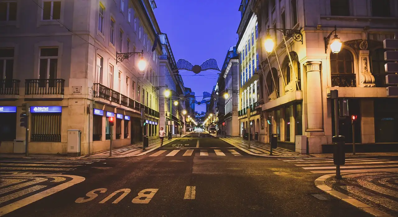 Lisbon's Baixa district street at dusk, with lit building facades and an empty road