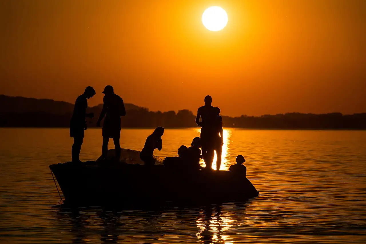 Silhouettes of people on a small boat against an orange sunset