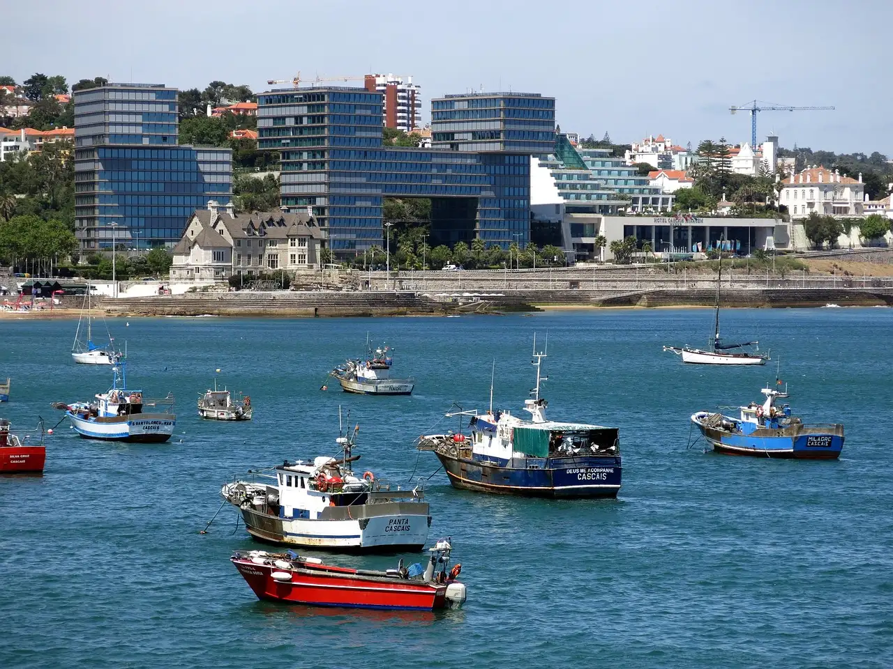 Colourful fishing boats moored in Cascais bay with the seafront behind
