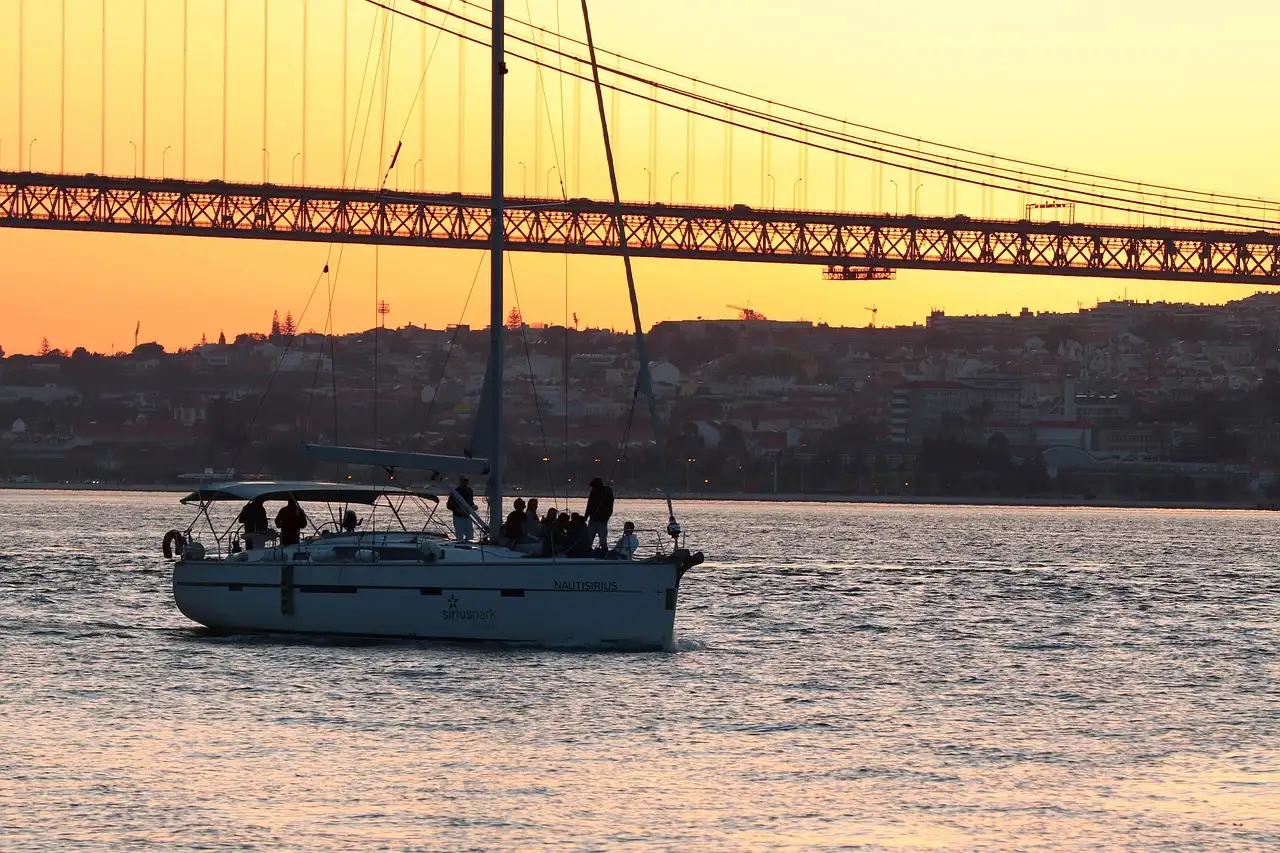 Sailing yacht on the Tagus in the evening light, passing beneath the 25 de Abril Bridge