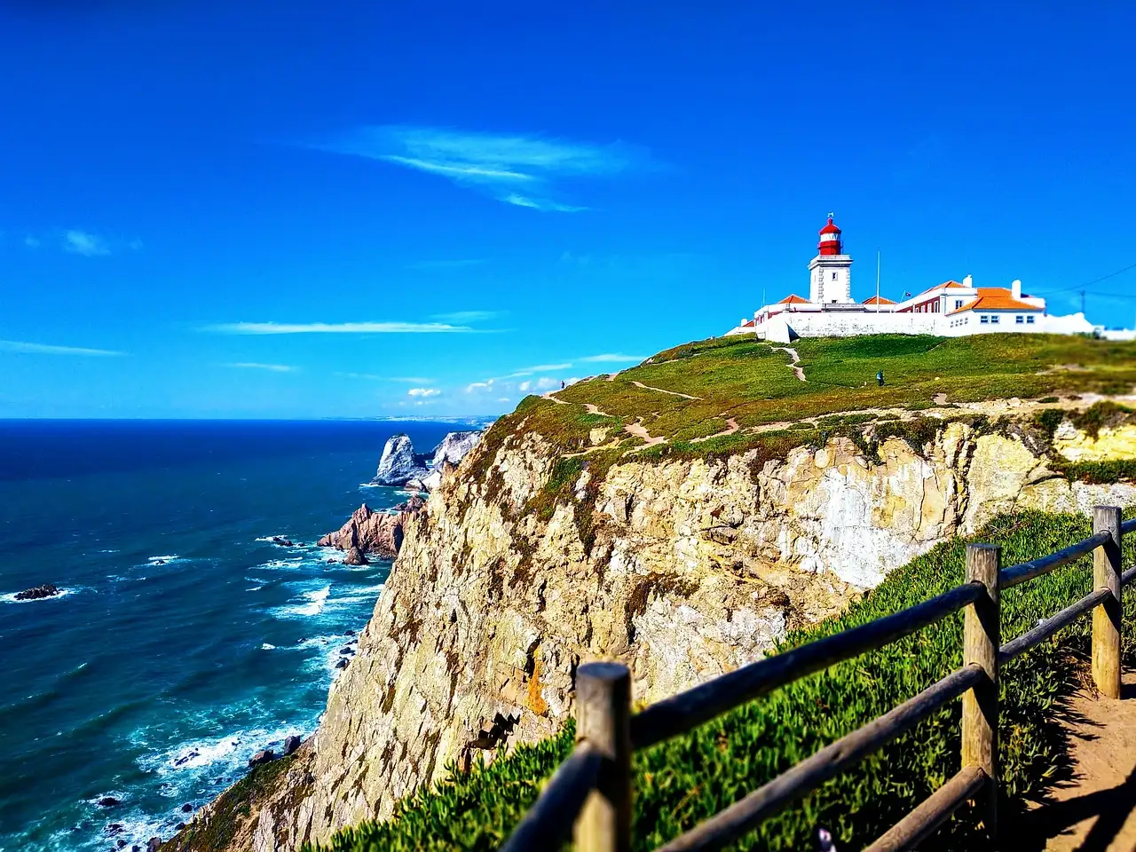 Cabo da Roca lighthouse on its grassy cliff above the deep blue Atlantic, with a wooden fence