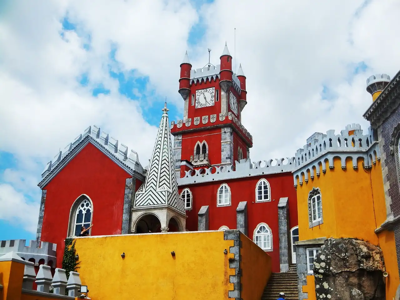 Red clock tower and patterned spire of Pena Palace above its yellow terrace walls