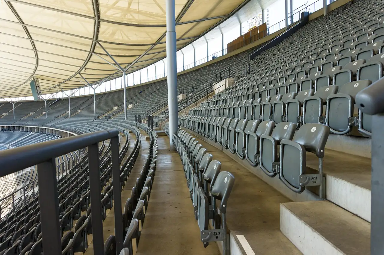 Rows of empty grey stadium seats beneath a white roof canopy