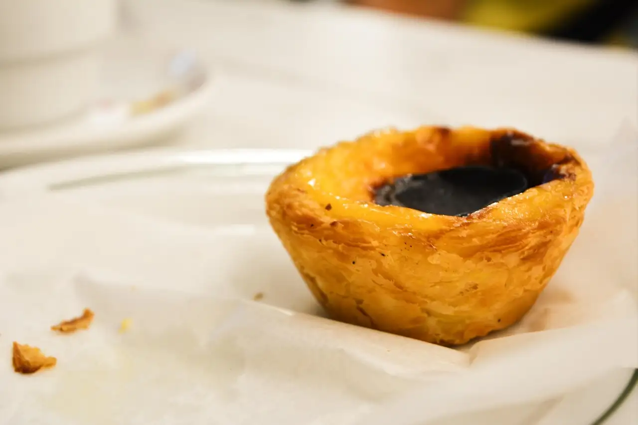 Single pastel de nata with a caramelised custard top resting on baking paper