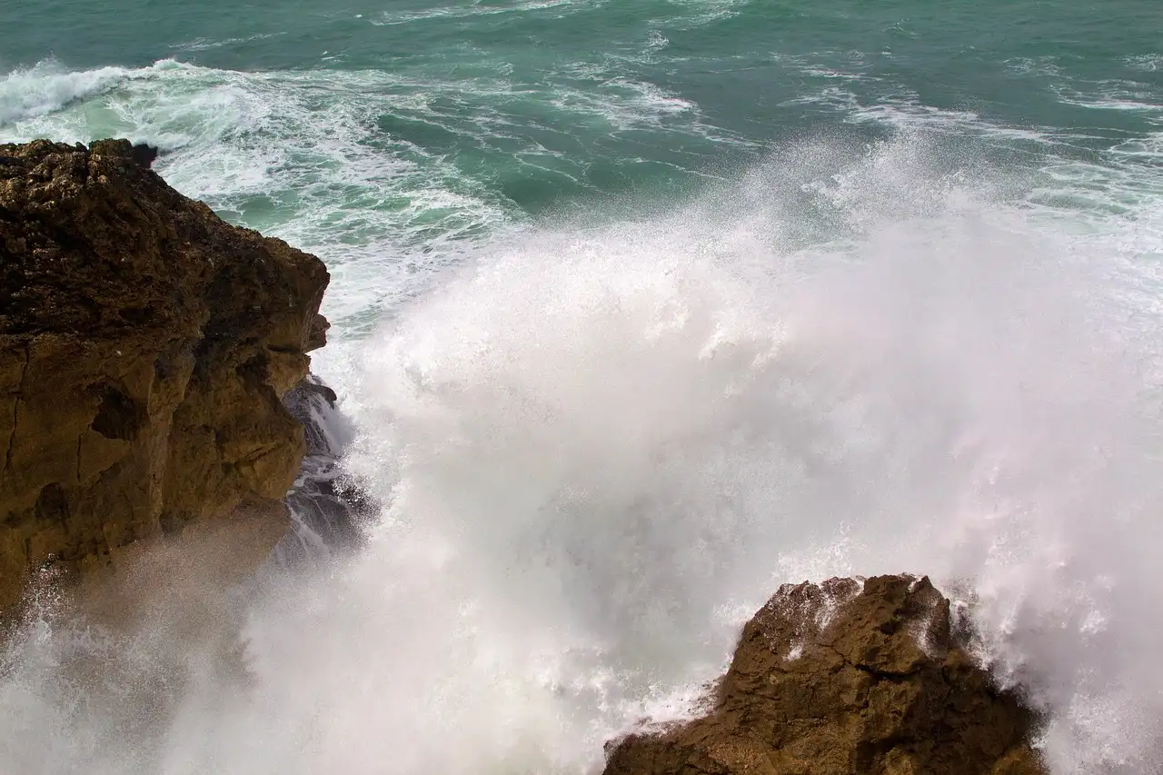 Powerful Atlantic wave crashing over dark rocks on the coast at Nazaré