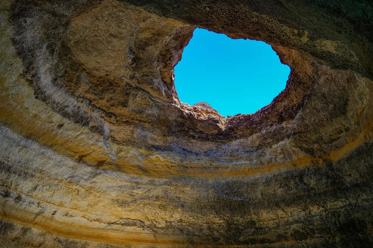 Looking up inside the Benagil cave at the round opening in its banded sandstone roof