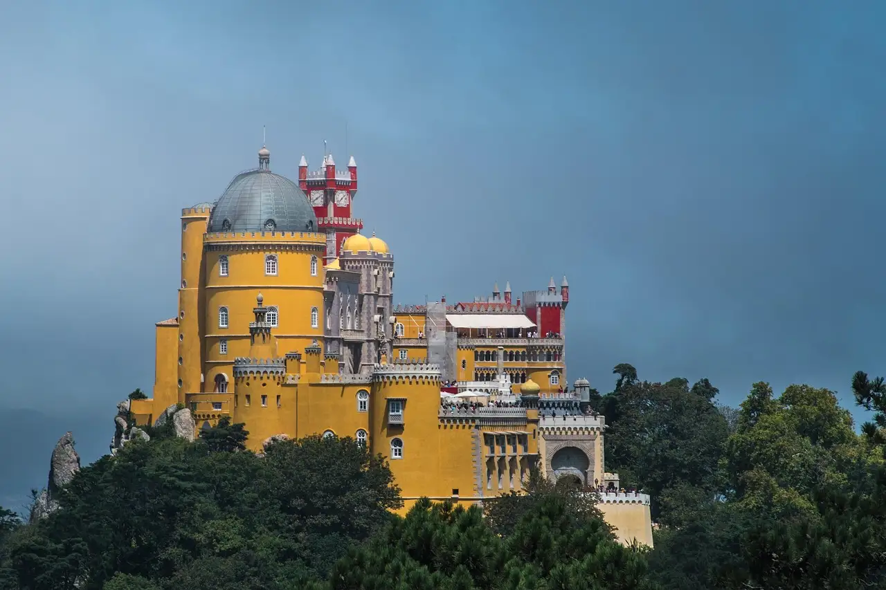 Pena Palace in Sintra with its yellow towers and red turret standing above dark pine forest under a stormy blue sky